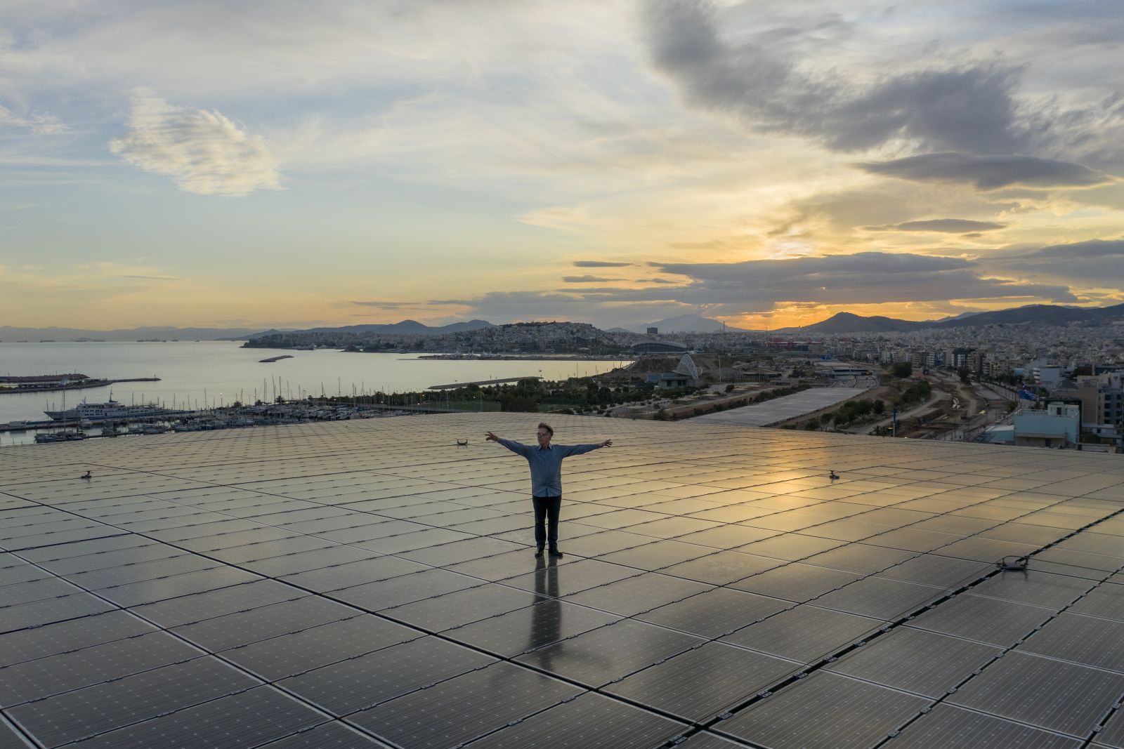 Φωτογραφία του συνθέτη Δημήτρη Καμαρωτού πάνω στο Ενεργειακό Στέγαστρο του ΚΠΙΣΝ, με θέα τη θάλασσα και τη μαγευτική δύση του ηλίου
