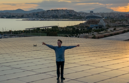 Φωτογραφία του συνθέτη Δημήτρη Καμαρωτού πάνω στο Ενεργειακό Στέγαστρο του ΚΠΙΣΝ με θέα τη θάλασσα και τη μαγευτική δύση του ηλίου