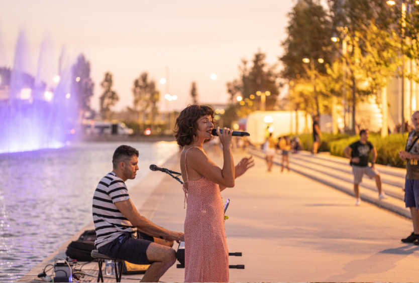 Φωτογραφία με μια γυναίκα που τραγουδάει και έναν άντρα που παίζει μουσική δίπλα στο Κανάλι