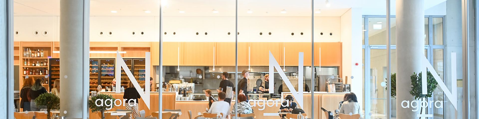 φωτογραφία του εστιατορίου Agora N, στο οποίο άτομα εργάζονται στην ανοιχτή κουζίνα ενώ οι επισκέπτες κάθονται στα τραπέζια